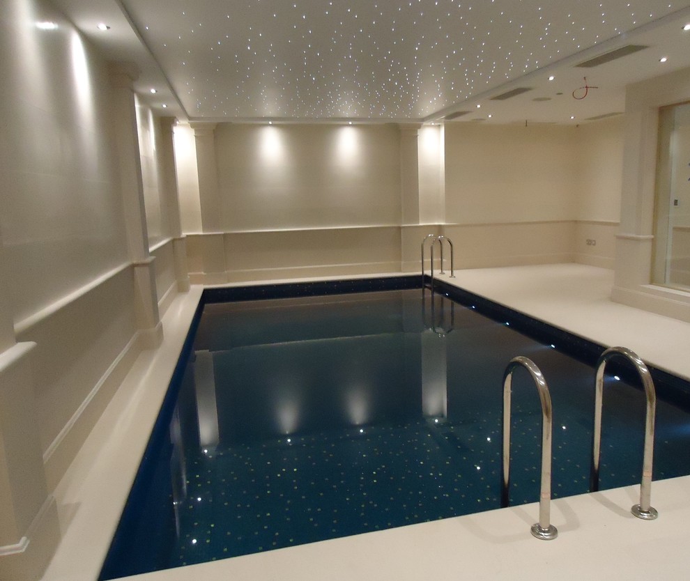 This is an example of a large contemporary indoor rectangular pool in London with a pool house and natural stone pavers.