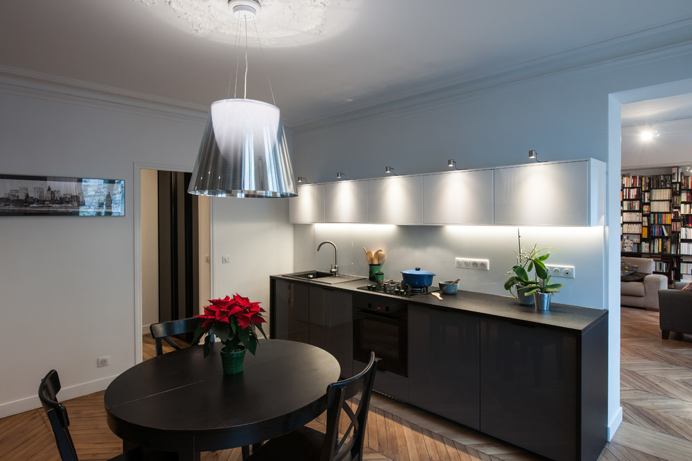 Inspiration for a mid-sized contemporary galley separate kitchen in Other with a single-bowl sink, beaded inset cabinets, grey cabinets, laminate benchtops, white splashback, porcelain splashback, black appliances, medium hardwood floors and no island.