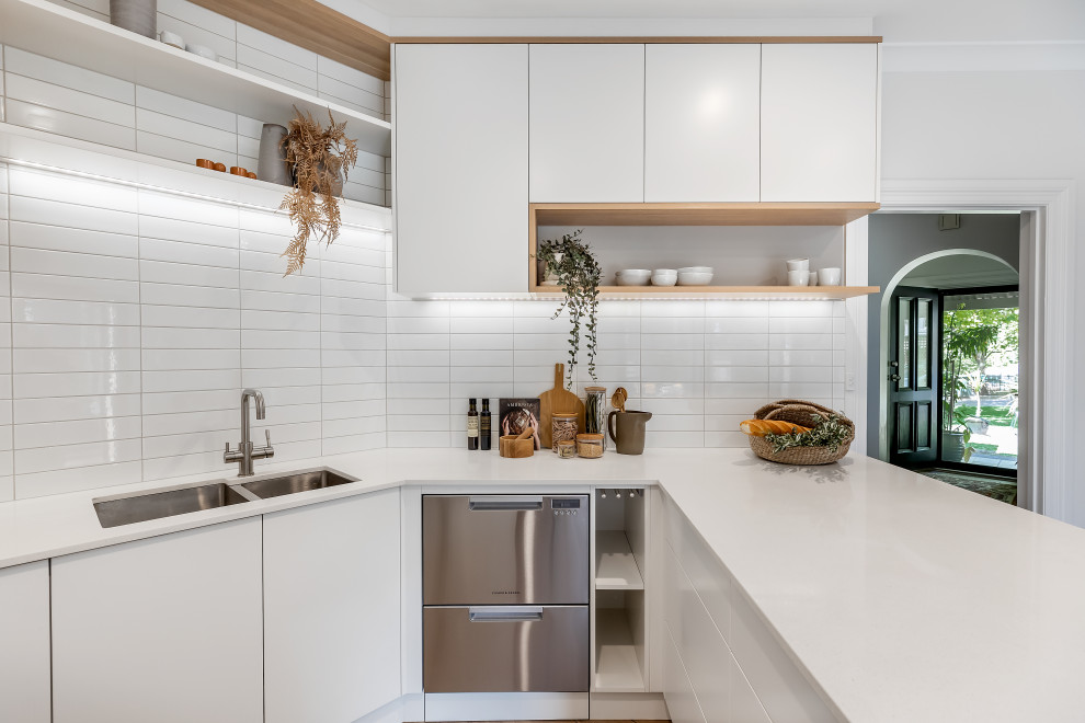 Exempel på ett litet modernt vit vitt kök, med en undermonterad diskho, släta luckor, vita skåp, bänkskiva i kvarts, vitt stänkskydd, stänkskydd i tunnelbanekakel, rostfria vitvaror, laminatgolv, en halv köksö och brunt golv
