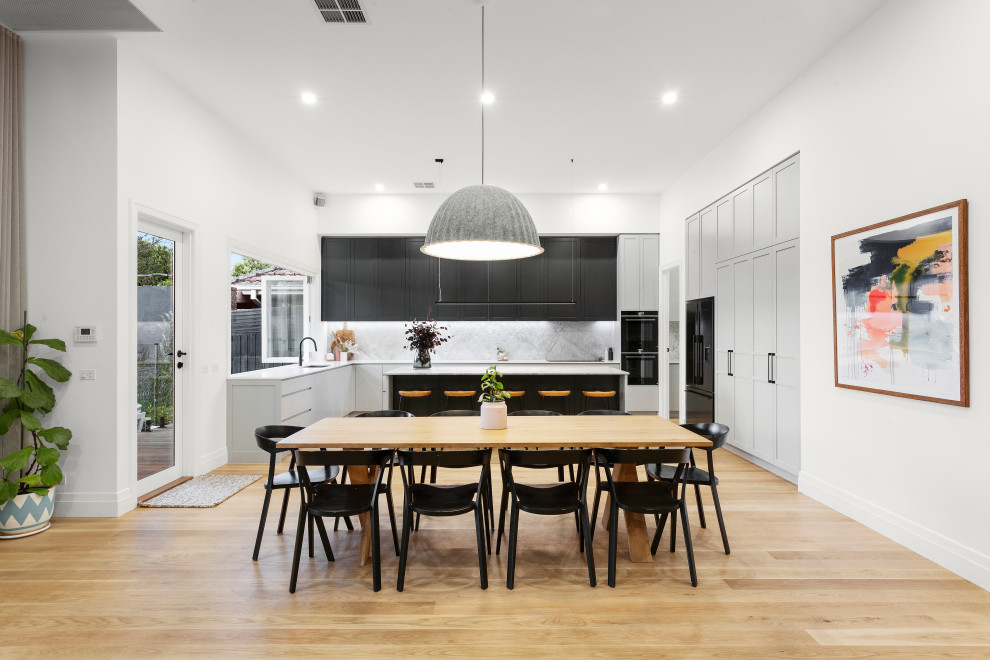Large contemporary u-shaped open plan kitchen in Melbourne with a double-bowl sink, shaker cabinets, marble benchtops, grey splashback, marble splashback, black appliances, light hardwood floors, with island and grey benchtop.