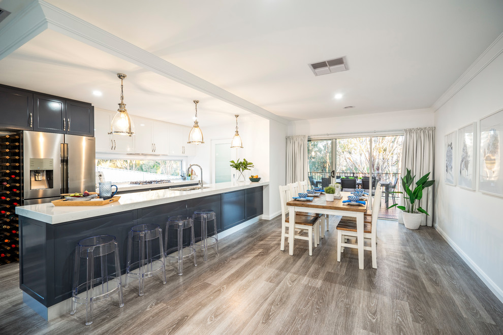 Photo of a mid-sized traditional galley eat-in kitchen in Other with an undermount sink, shaker cabinets, blue cabinets, quartz benchtops, metallic splashback, window splashback, stainless steel appliances, linoleum floors, with island, grey floor and white benchtop.