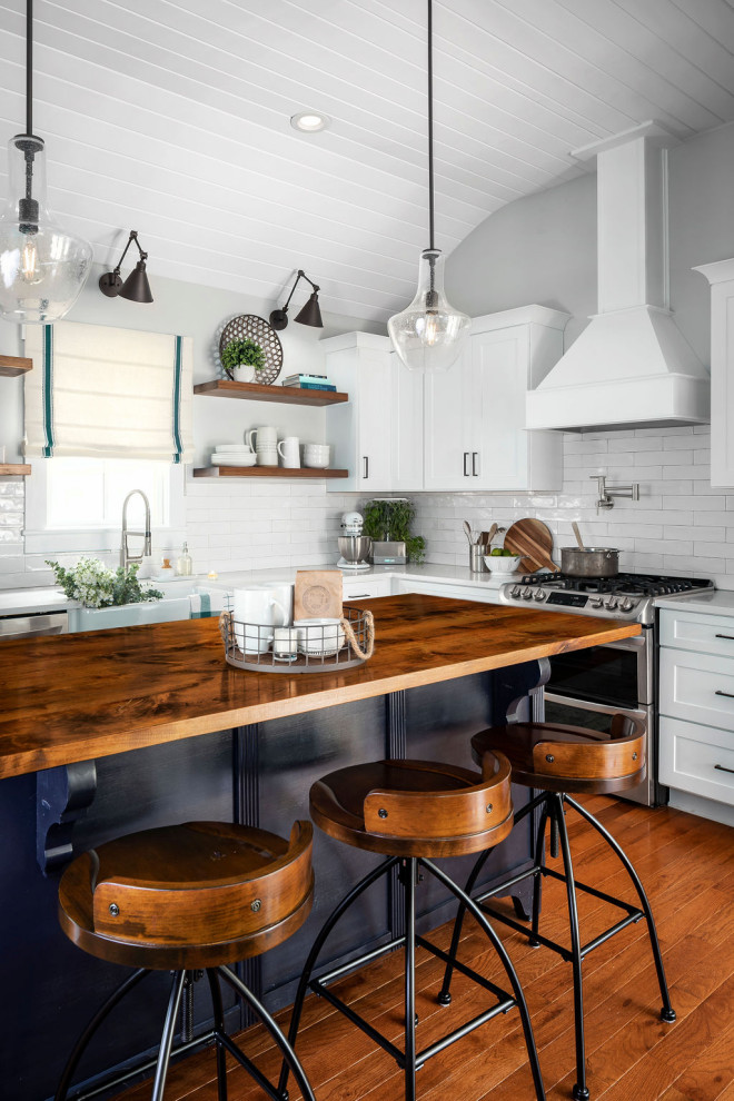 Design ideas for a mid-sized country l-shaped eat-in kitchen in Orlando with a farmhouse sink, shaker cabinets, white cabinets, quartz benchtops, white splashback, ceramic splashback, stainless steel appliances, medium hardwood floors, with island, brown floor and white benchtop.