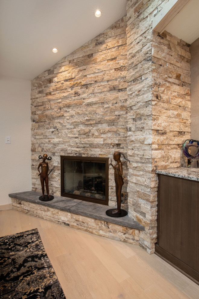 Exemple d'une salle de séjour tendance de taille moyenne et ouverte avec un mur beige, parquet clair, une cheminée d'angle, un manteau de cheminée en pierre de parement, un sol marron, un plafond voûté et du lambris.