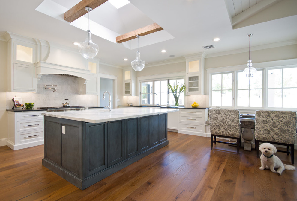 Large transitional u-shaped medium tone wood floor eat-in kitchen photo in Phoenix with a farmhouse sink, recessed-panel cabinets, white cabinets, marble countertops, white backsplash, stone tile backsplash, stainless steel appliances and an island