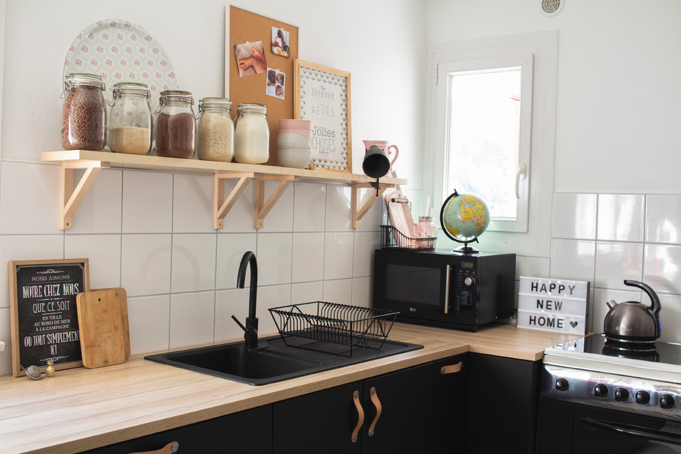 Exemple d'une cuisine industrielle fermée et de taille moyenne avec un évier 1 bac, des portes de placard noires, un plan de travail en stratifié, une crédence blanche, un électroménager en acier inoxydable et un sol blanc.