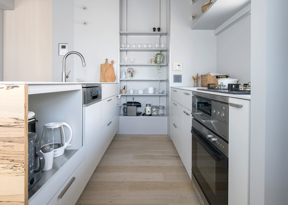 This is an example of a scandinavian galley open plan kitchen in Tokyo with an undermount sink, beaded inset cabinets, white cabinets, white splashback, stainless steel appliances, light hardwood floors, a peninsula, beige floor and white benchtop.