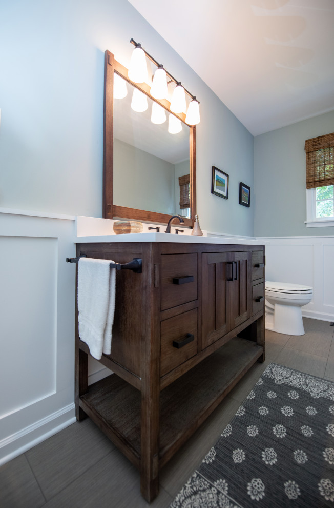 Photo of a mid-sized country bathroom in Philadelphia with furniture-like cabinets, brown cabinets, a freestanding tub, an alcove shower, a two-piece toilet, white tile, porcelain tile, green walls, porcelain floors, an undermount sink, engineered quartz benchtops, grey floor, a hinged shower door, white benchtops, a niche, a single vanity, a freestanding vanity and decorative wall panelling.