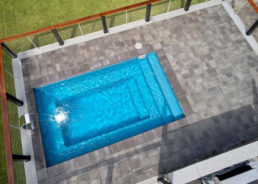 Ejemplo de piscina con fuente moderna pequeña rectangular en patio trasero con adoquines de ladrillo