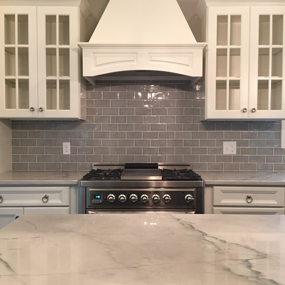 This is an example of a mid-sized transitional l-shaped eat-in kitchen in Boston with a farmhouse sink, flat-panel cabinets, white cabinets, quartzite benchtops, grey splashback, porcelain splashback, stainless steel appliances, dark hardwood floors and with island.