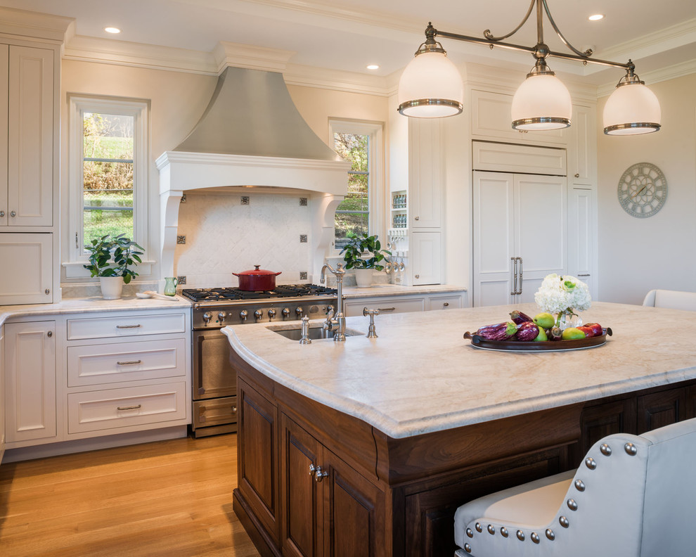 This is an example of a large transitional l-shaped open plan kitchen in Philadelphia with an undermount sink, beaded inset cabinets, white cabinets, marble benchtops, beige splashback, stone tile splashback, panelled appliances, medium hardwood floors and with island.