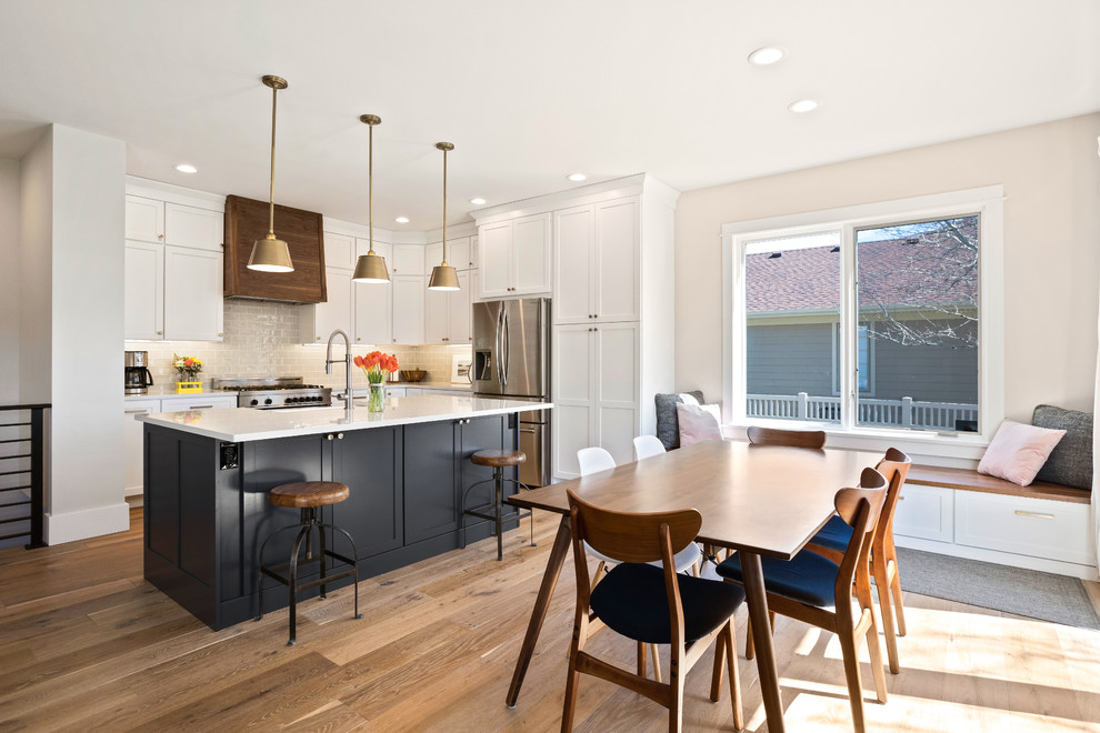 Kitchen - transitional l-shaped light wood floor and brown floor kitchen idea with a farmhouse sink, shaker cabinets, white cabinets, quartz countertops, white backsplash, subway tile backsplash, stainless steel appliances, an island and white countertops