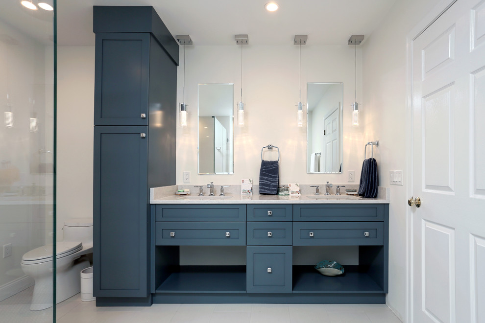 This is an example of a mid-sized transitional master bathroom in Boston with shaker cabinets, blue cabinets, a corner shower, a two-piece toilet, white tile, porcelain tile, white walls, porcelain floors, an undermount sink, engineered quartz benchtops, white floor, a hinged shower door and white benchtops.
