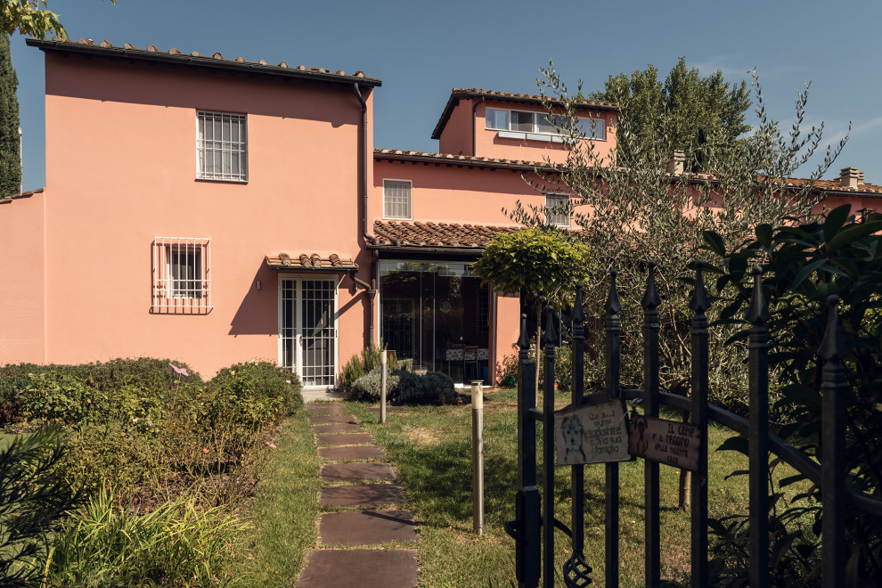 This is an example of a large contemporary one-storey stucco pink apartment exterior in Florence with a gable roof, a tile roof and a red roof.
