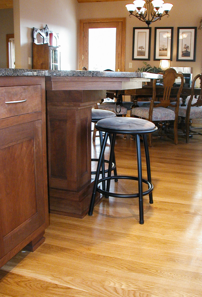 Mid-sized l-shaped eat-in kitchen photo with an undermount sink, shaker cabinets, dark wood cabinets, granite countertops, stainless steel appliances and an island