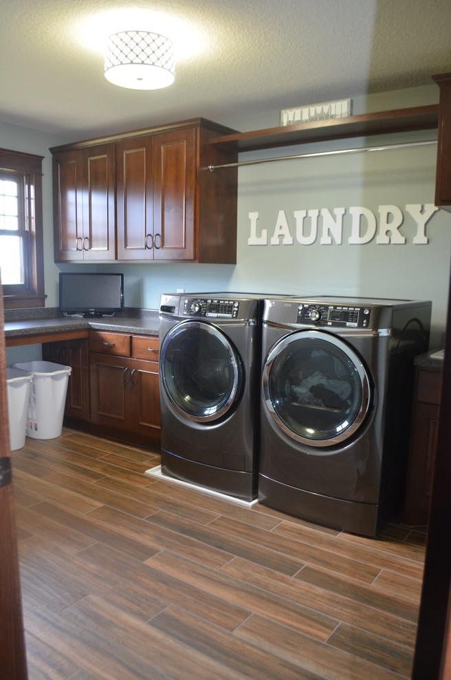 Design ideas for a mid-sized traditional l-shaped dedicated laundry room in Minneapolis with a drop-in sink, recessed-panel cabinets, dark wood cabinets, solid surface benchtops, blue walls, laminate floors and a side-by-side washer and dryer.