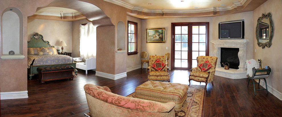 Inspiration for a large mediterranean master bedroom in Los Angeles with brown walls, dark hardwood floors, a corner fireplace, a stone fireplace surround and brown floor.