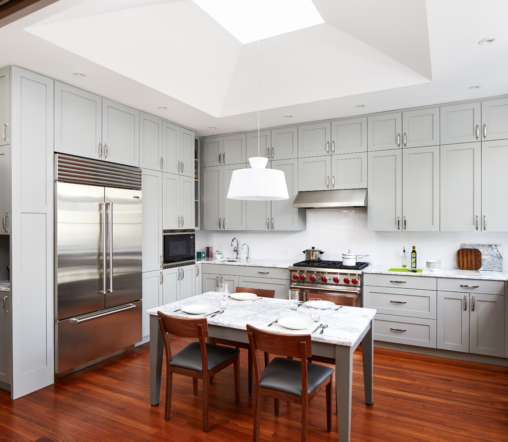 Design ideas for a transitional eat-in kitchen in DC Metro with shaker cabinets, grey cabinets, white splashback, stainless steel appliances, medium hardwood floors, no island and brown floor.