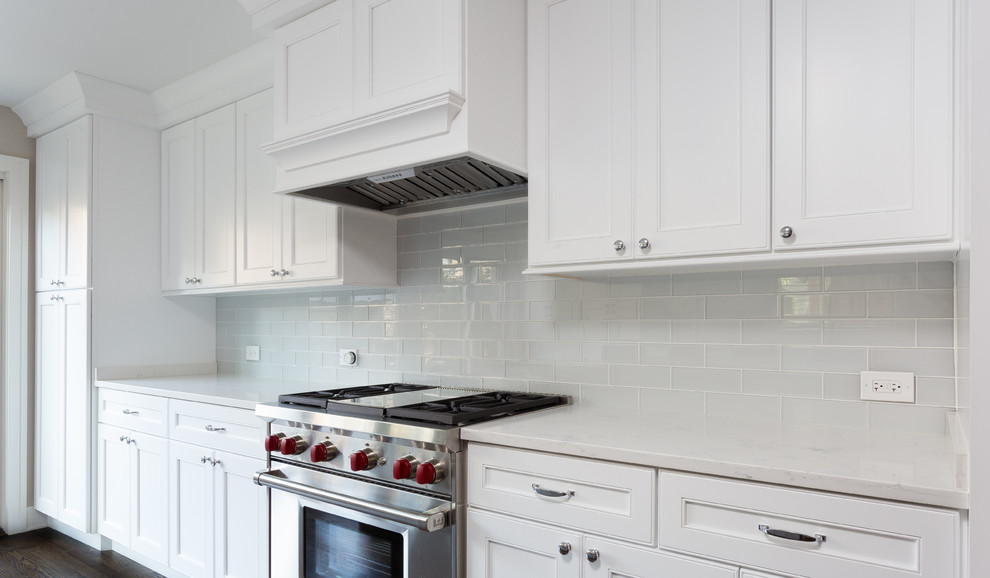 Inspiration for a large transitional galley dark wood floor kitchen remodel in Chicago with an undermount sink, shaker cabinets, white cabinets, quartzite countertops, white backsplash, glass tile backsplash, stainless steel appliances and an island