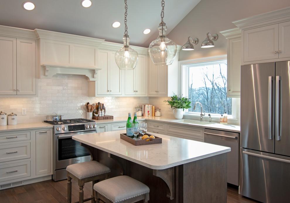 Transitional medium tone wood floor, brown floor and vaulted ceiling eat-in kitchen photo with an undermount sink, shaker cabinets, white cabinets, quartz countertops, white backsplash, ceramic backsplash, stainless steel appliances, an island and white countertops
