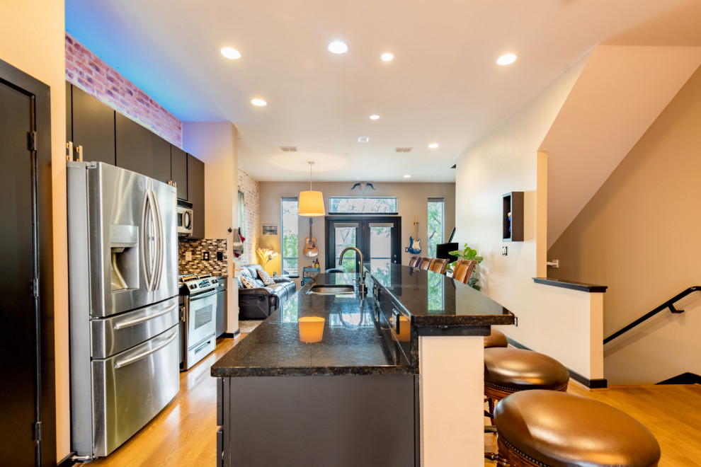 Photo of a large urban galley open plan kitchen in Dallas with a submerged sink, flat-panel cabinets, grey cabinets, granite worktops, multi-coloured splashback, mosaic tiled splashback, stainless steel appliances, light hardwood flooring, an island, yellow floors and black worktops.