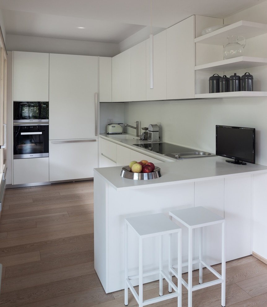 Inspiration for a mid-sized modern eat-in kitchen in Milan with an integrated sink, solid surface benchtops, white splashback, stainless steel appliances, painted wood floors, a peninsula and beige floor.
