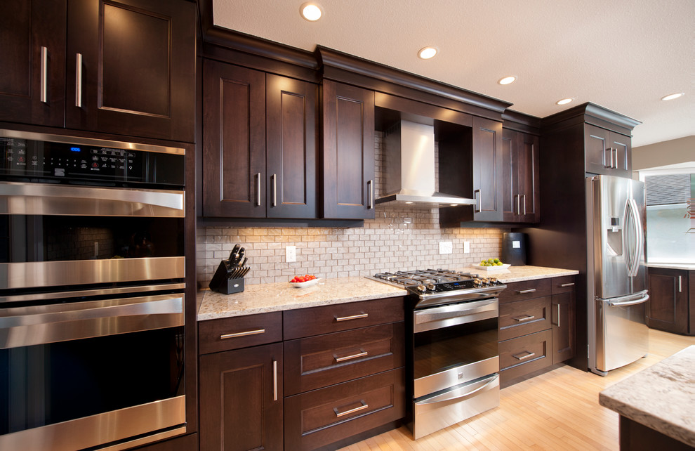 Eat-in kitchen - large u-shaped light wood floor eat-in kitchen idea in Vancouver with an undermount sink, recessed-panel cabinets, dark wood cabinets, glass tile backsplash, stainless steel appliances and an island