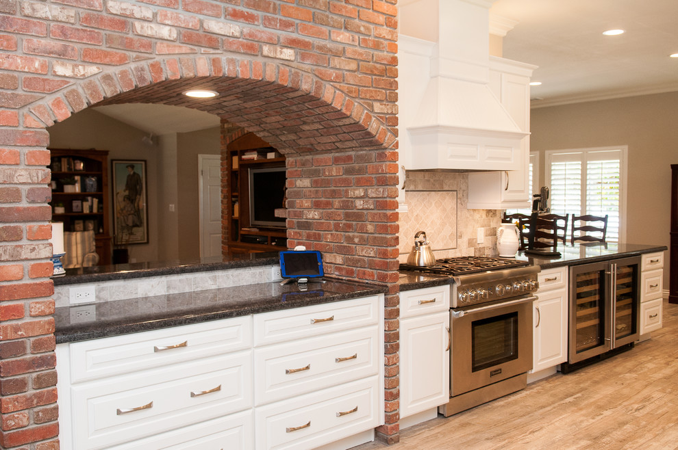 Inspiration for a mid-sized transitional galley porcelain tile and beige floor enclosed kitchen remodel with a triple-bowl sink, raised-panel cabinets, white cabinets, granite countertops, beige backsplash, porcelain backsplash, stainless steel appliances and a peninsula