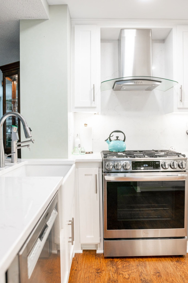This is an example of a small traditional u-shaped enclosed kitchen in Minneapolis with a belfast sink, shaker cabinets, white cabinets, engineered stone countertops, white splashback, engineered quartz splashback, stainless steel appliances, vinyl flooring, no island, brown floors and white worktops.