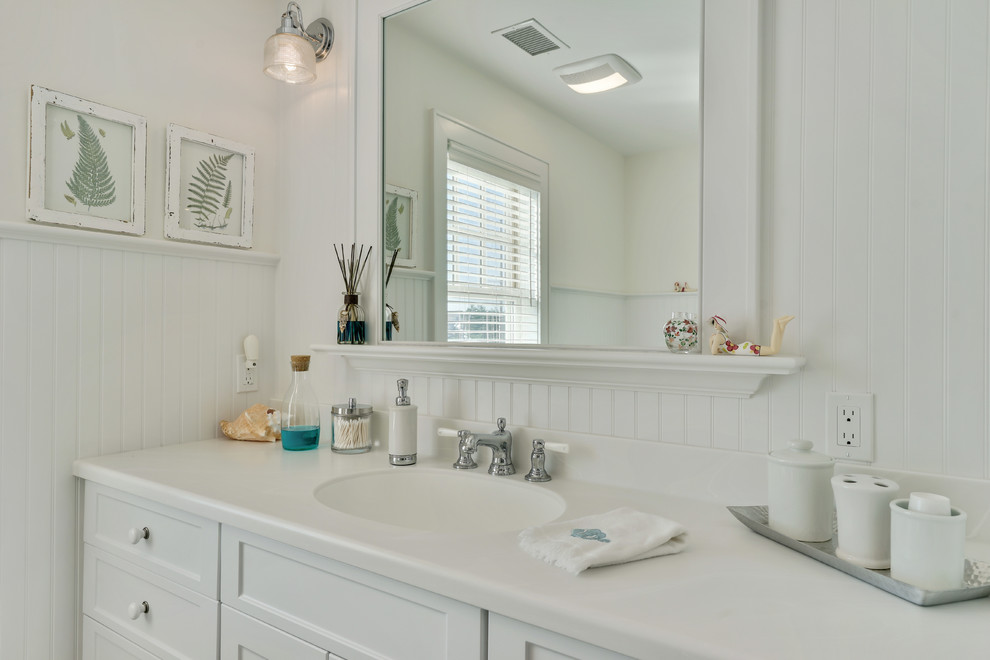 This is an example of a beach style bathroom in New York with recessed-panel cabinets, white cabinets, a corner shower, white tile, subway tile, white walls, marble floors and an integrated sink.