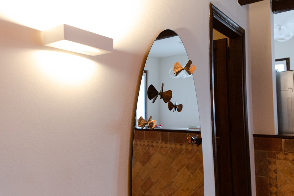 Idée de décoration pour un grand hall d'entrée champêtre avec un mur blanc, tomettes au sol, une porte simple, une porte blanche, un sol marron et poutres apparentes.
