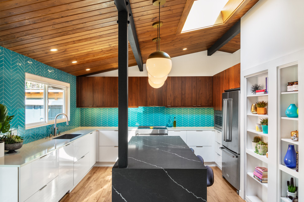 Bild på ett stort retro svart svart kök, med en undermonterad diskho, släta luckor, skåp i mörkt trä, bänkskiva i kvarts, blått stänkskydd, stänkskydd i keramik, rostfria vitvaror, ljust trägolv, en köksö och brunt golv