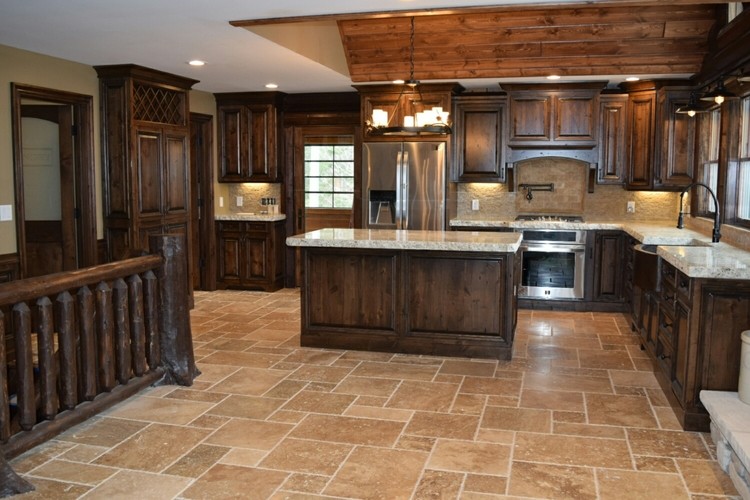 Mid-sized mountain style l-shaped travertine floor and brown floor enclosed kitchen photo in Chicago with a farmhouse sink, raised-panel cabinets, dark wood cabinets, granite countertops, stainless steel appliances, an island and white countertops