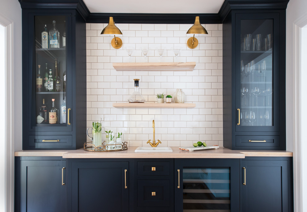 Inspiration for a small traditional single-wall wet bar in New York with a drop-in sink, shaker cabinets, blue cabinets, wood benchtops, white splashback and subway tile splashback.