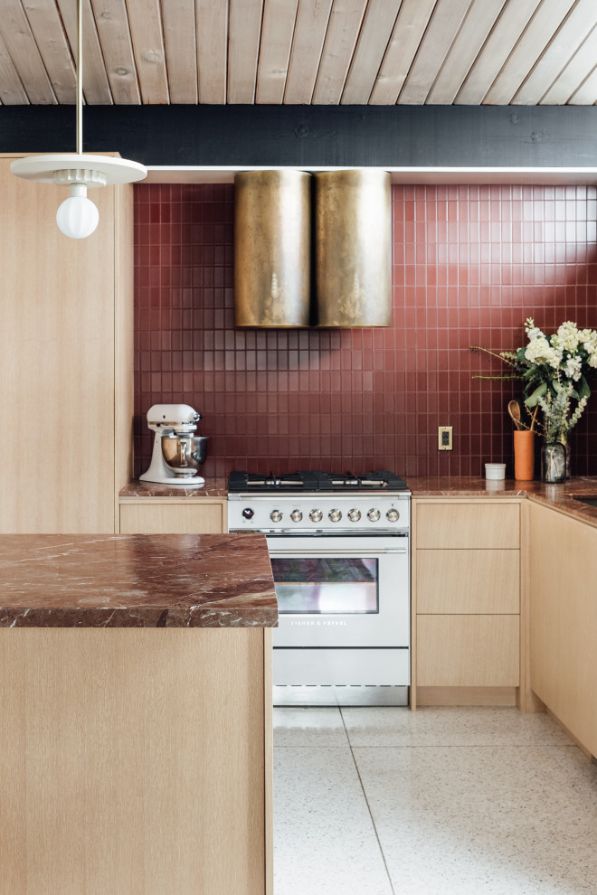 На фото: угловая кухня среднего размера в стиле ретро с обеденным столом, монолитной мойкой, плоскими фасадами, светлыми деревянными фасадами, мраморной столешницей, красным фартуком, фартуком из стеклянной плитки, белой техникой, полом из терраццо, полуостровом, серым полом, красной столешницей и балками на потолке с