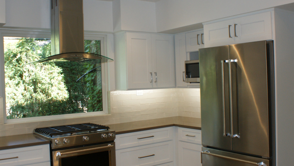 Photo of a mid-sized traditional u-shaped separate kitchen in Chicago with an undermount sink, shaker cabinets, white cabinets, quartz benchtops, beige splashback, subway tile splashback, stainless steel appliances, vinyl floors, no island, beige floor and beige benchtop.