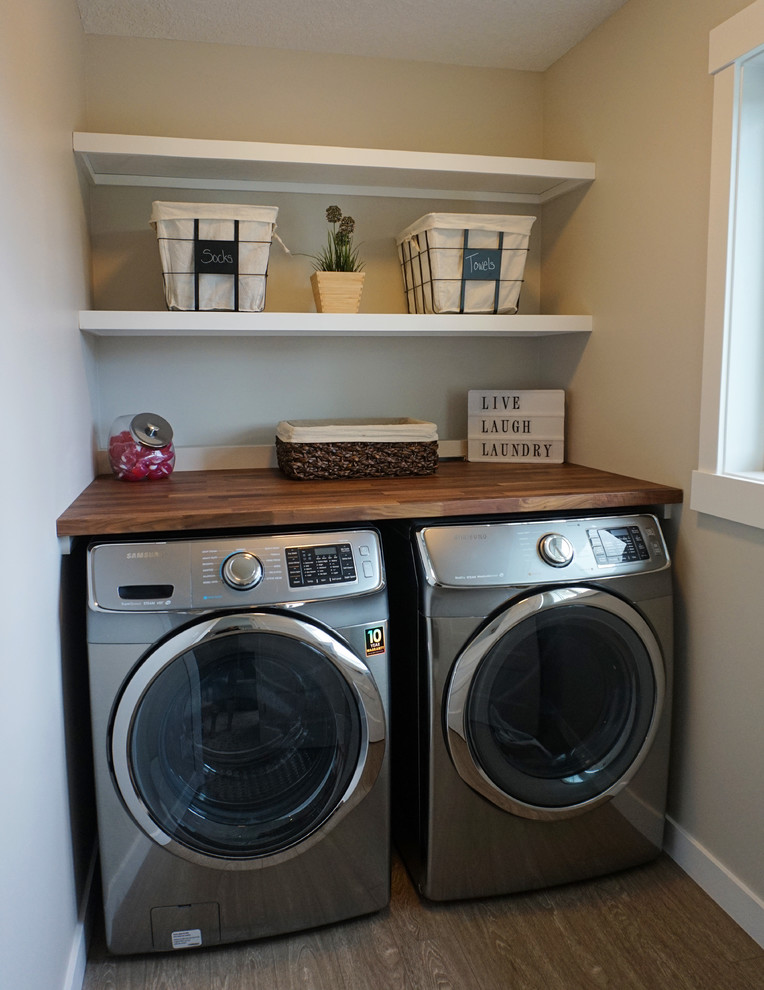 Design ideas for a small transitional single-wall laundry cupboard in Calgary with wood benchtops, beige walls, medium hardwood floors and a side-by-side washer and dryer.