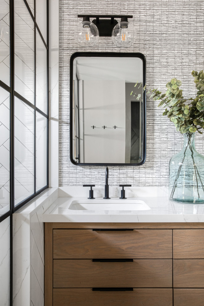 This is an example of a mid-sized contemporary master bathroom in Orange County with flat-panel cabinets, light wood cabinets, a corner shower, white tile, subway tile, grey walls, porcelain floors, an undermount sink, marble benchtops, black floor, a hinged shower door, white benchtops, an enclosed toilet, a double vanity, a freestanding vanity and wallpaper.