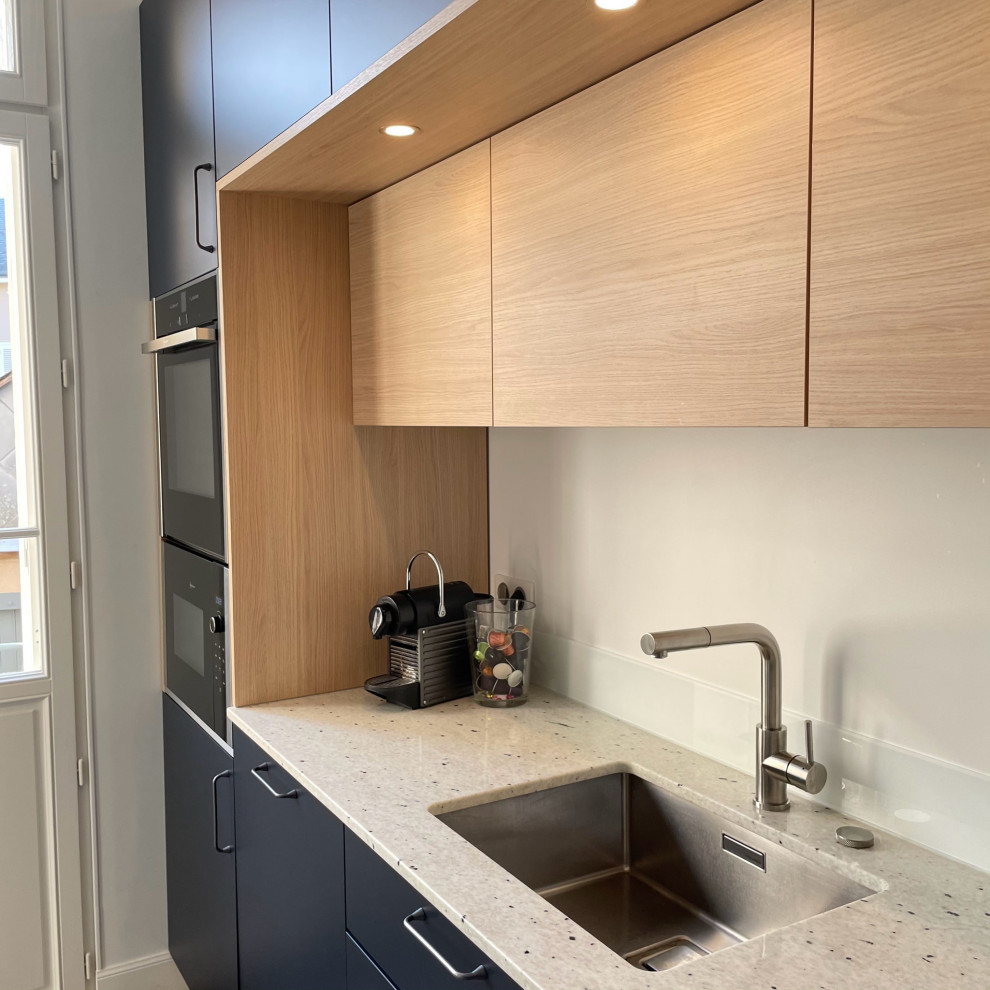 Exemple d'une cuisine bicolore en L fermée et de taille moyenne avec un évier encastré, un placard à porte affleurante, des portes de placard bleues, un plan de travail en granite, une crédence blanche, une crédence en feuille de verre, un électroménager en acier inoxydable, carreaux de ciment au sol, aucun îlot, un sol multicolore et un plan de travail blanc.