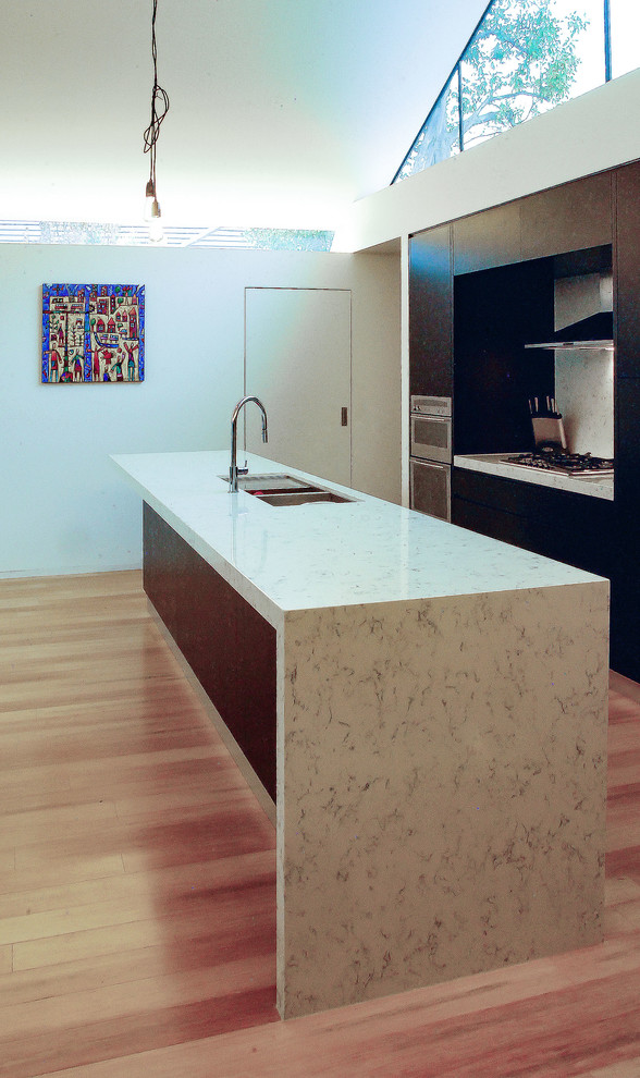 Photo of a mid-sized contemporary galley open plan kitchen in Adelaide with an undermount sink, flat-panel cabinets, black cabinets, quartz benchtops, white splashback, stone slab splashback, stainless steel appliances, bamboo floors, with island, beige floor and white benchtop.