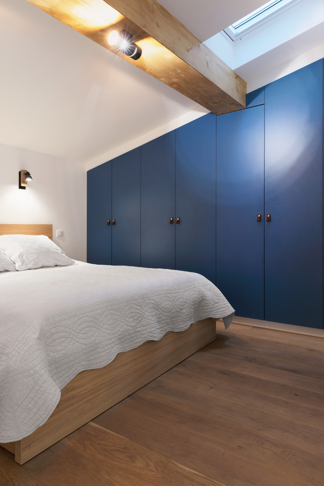 Cette photo montre une chambre mansardée ou avec mezzanine industrielle de taille moyenne avec un mur blanc et parquet clair.