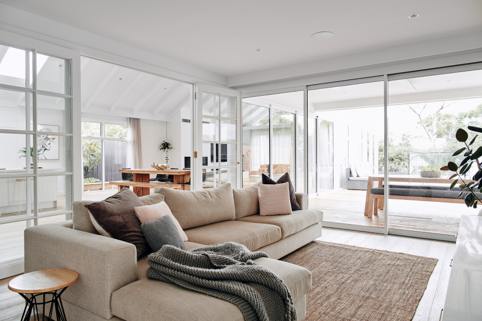 Photo of a large beach style formal open concept living room in Melbourne with white walls, light hardwood floors, a standard fireplace, a plaster fireplace surround, a wall-mounted tv, beige floor, recessed and panelled walls.