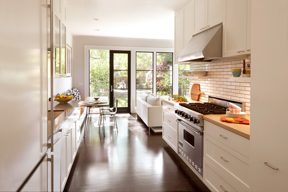 Design ideas for a mid-sized contemporary galley eat-in kitchen in San Francisco with white cabinets, white splashback, stainless steel appliances, dark hardwood floors, flat-panel cabinets, wood benchtops, subway tile splashback, no island, an undermount sink and brown floor.