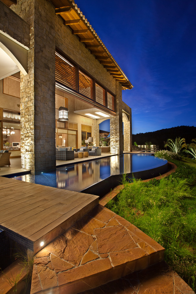 Photo of a contemporary custom-shaped infinity pool in Other with natural stone pavers.