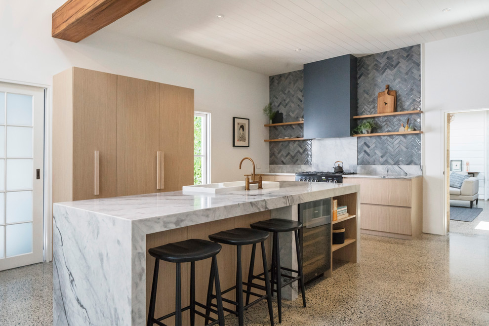 Design ideas for a country l-shaped kitchen in Sydney with a drop-in sink, flat-panel cabinets, light wood cabinets, grey splashback, black appliances, concrete floors, with island, beige floor and grey benchtop.