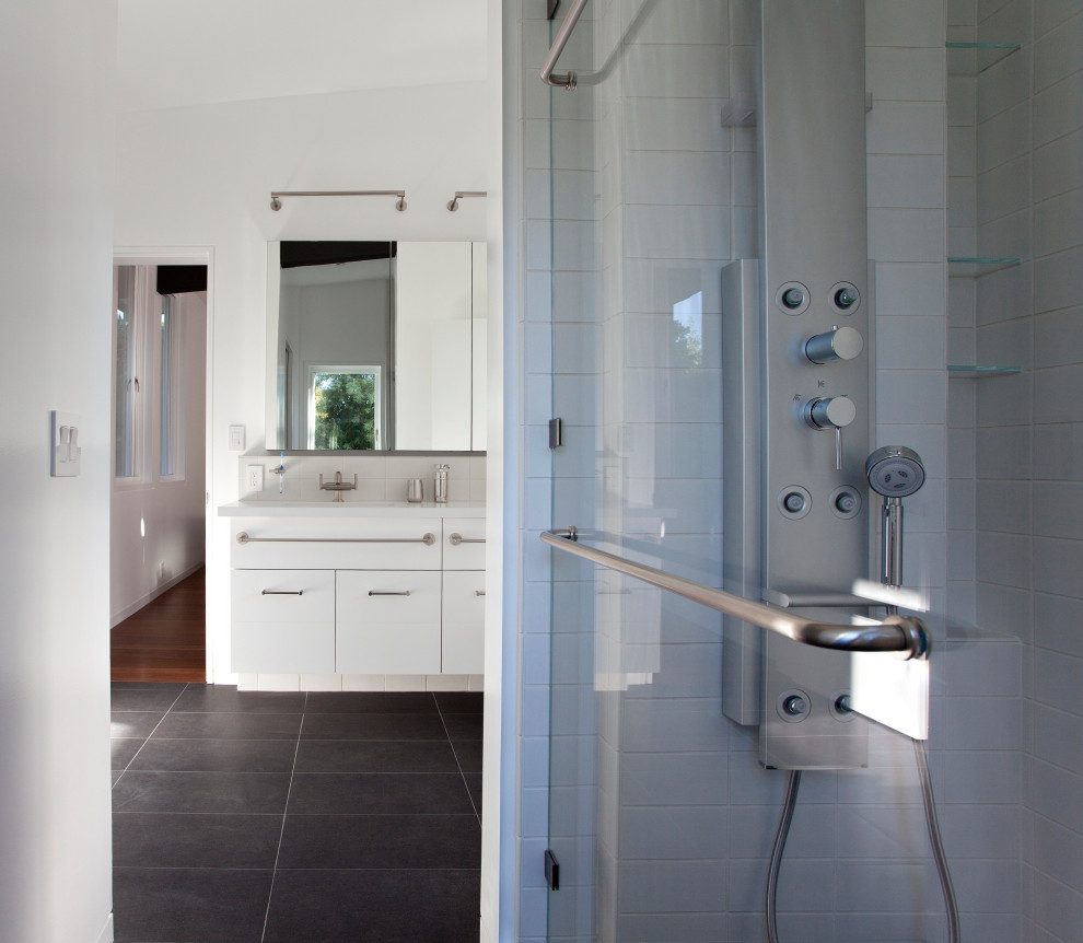 This is an example of a contemporary master bathroom in San Francisco with flat-panel cabinets, white cabinets, white walls, porcelain floors, an undermount sink, black floor, a hinged shower door, white benchtops, a double vanity and a floating vanity.