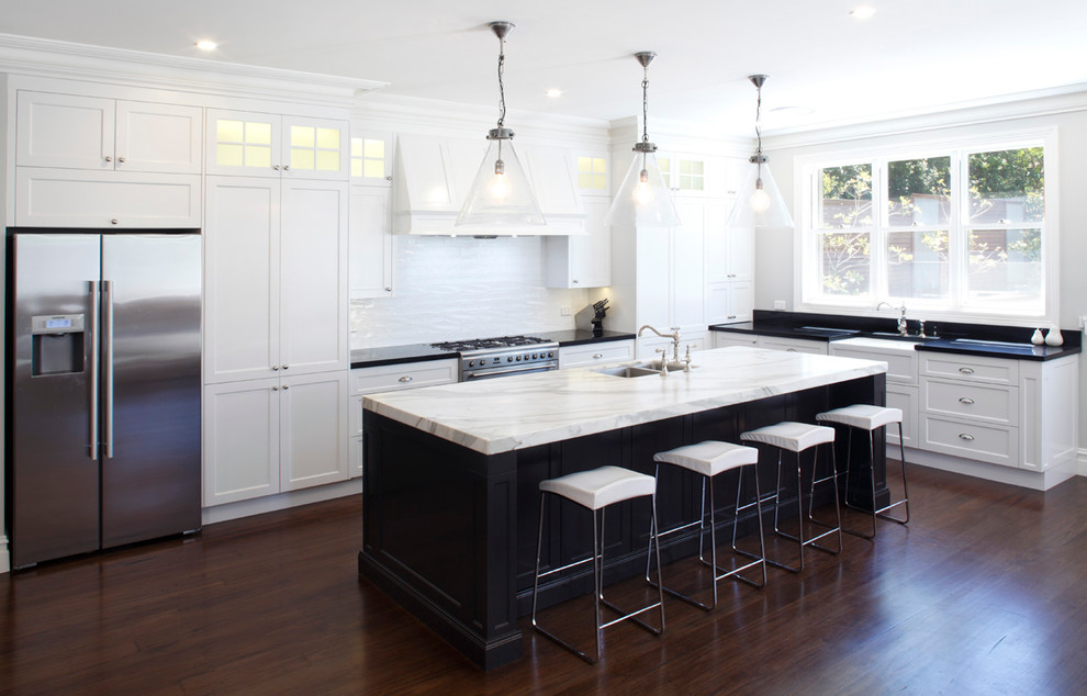 Mid-sized elegant l-shaped dark wood floor open concept kitchen photo in Sydney with a farmhouse sink, shaker cabinets, white cabinets, marble countertops, white backsplash, ceramic backsplash, stainless steel appliances and an island