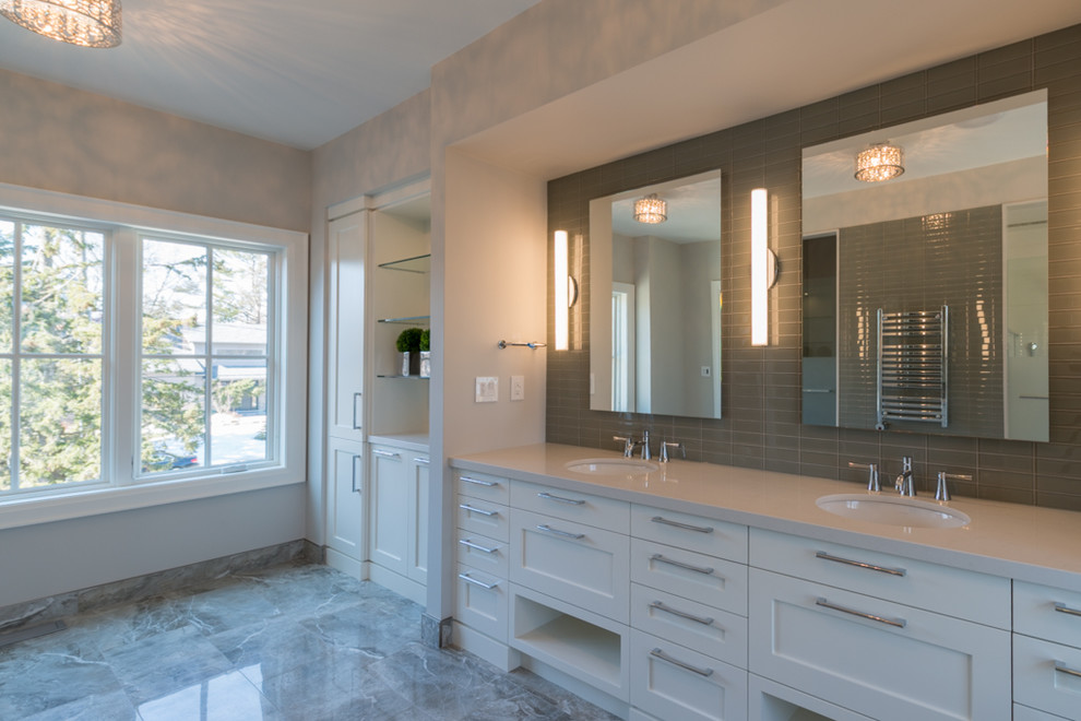 This is an example of a large contemporary master bathroom in Toronto with an undermount sink, shaker cabinets, white cabinets, solid surface benchtops, a freestanding tub, an alcove shower, a one-piece toilet, gray tile, porcelain tile, grey walls and porcelain floors.