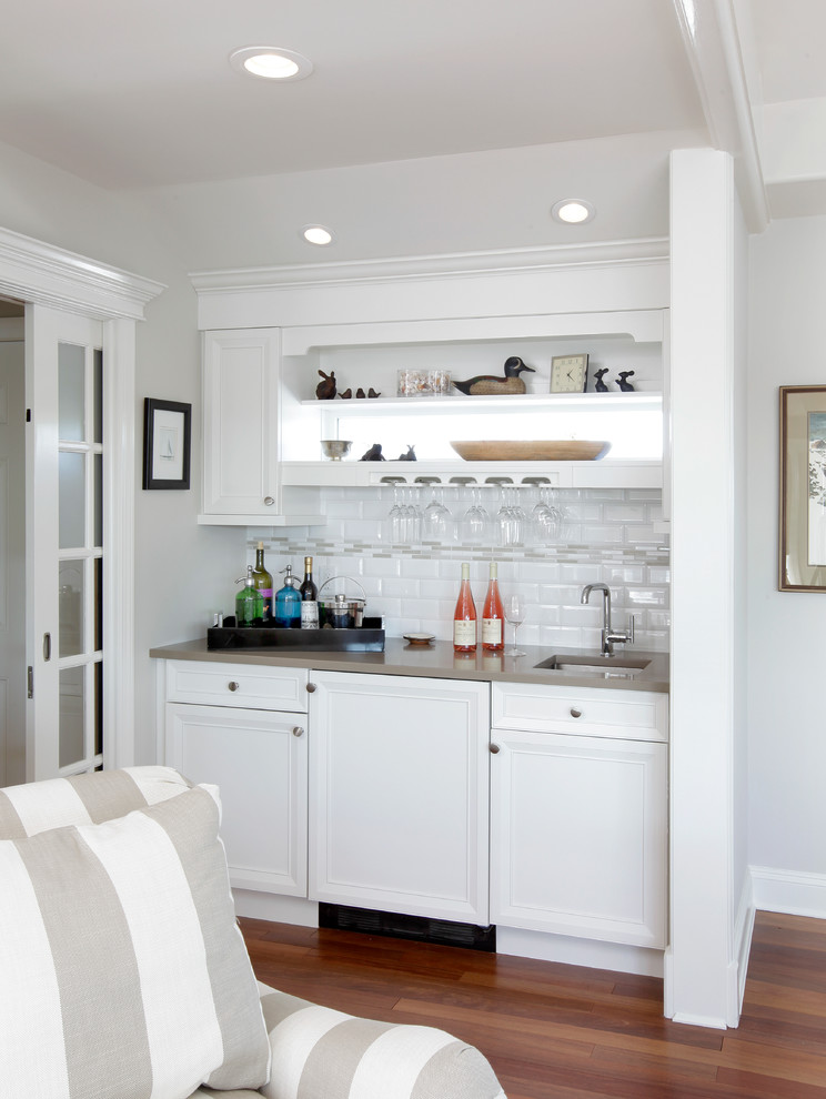 Small transitional single-wall wet bar in New York with an undermount sink, recessed-panel cabinets, white cabinets, white splashback, subway tile splashback and medium hardwood floors.