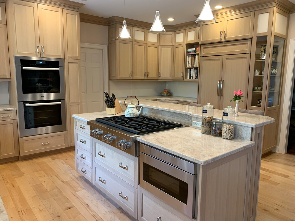 This is an example of a large country eat-in kitchen in New York with a drop-in sink, shaker cabinets, beige cabinets, limestone benchtops, white splashback, cement tile splashback, stainless steel appliances, light hardwood floors, with island, beige floor and beige benchtop.