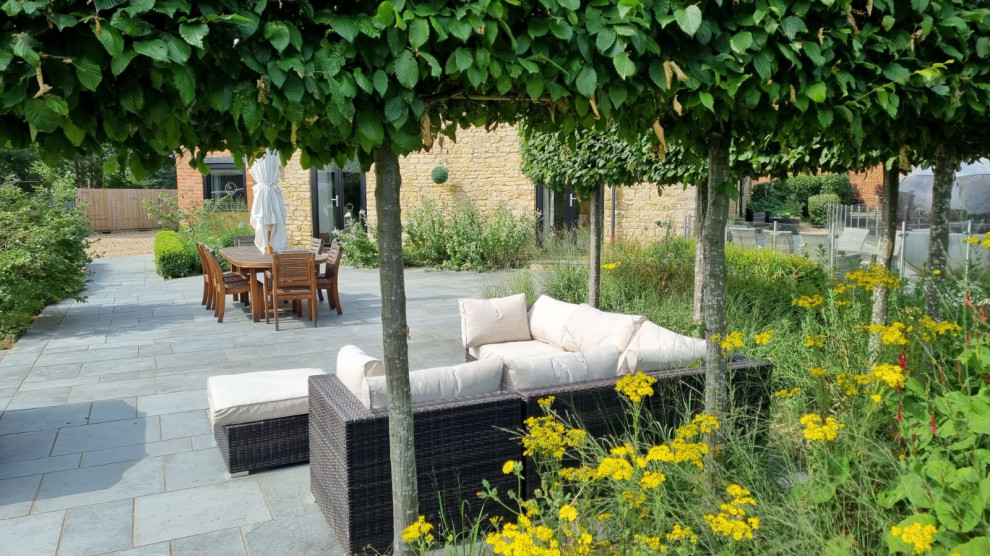 Expansive contemporary formal garden in Buckinghamshire with a retaining wall and natural stone pavers.